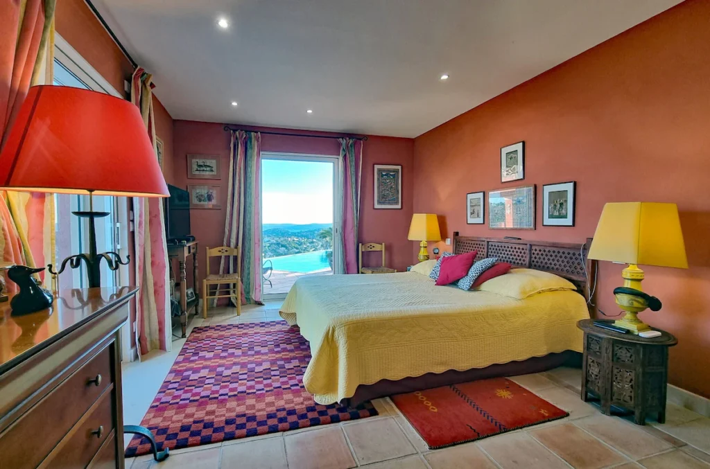 Chambre lumineuse décorée dans des tons chauds, avec lit double et large baie vitrée offrant une vue extérieure.